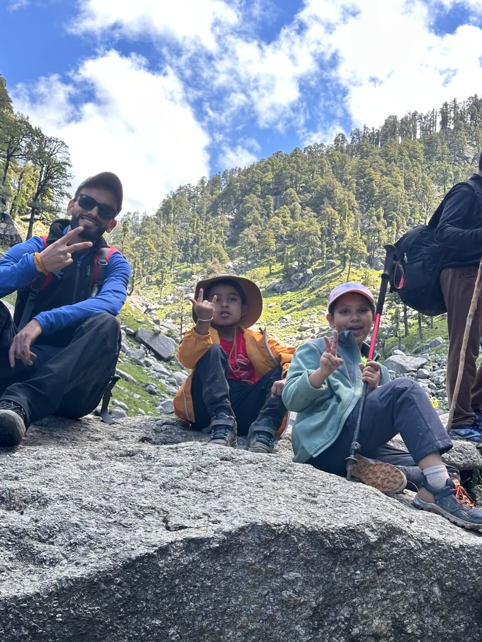 Yuvan, his friend Zayra and the trek guide sitting on a big rock posing for a photo