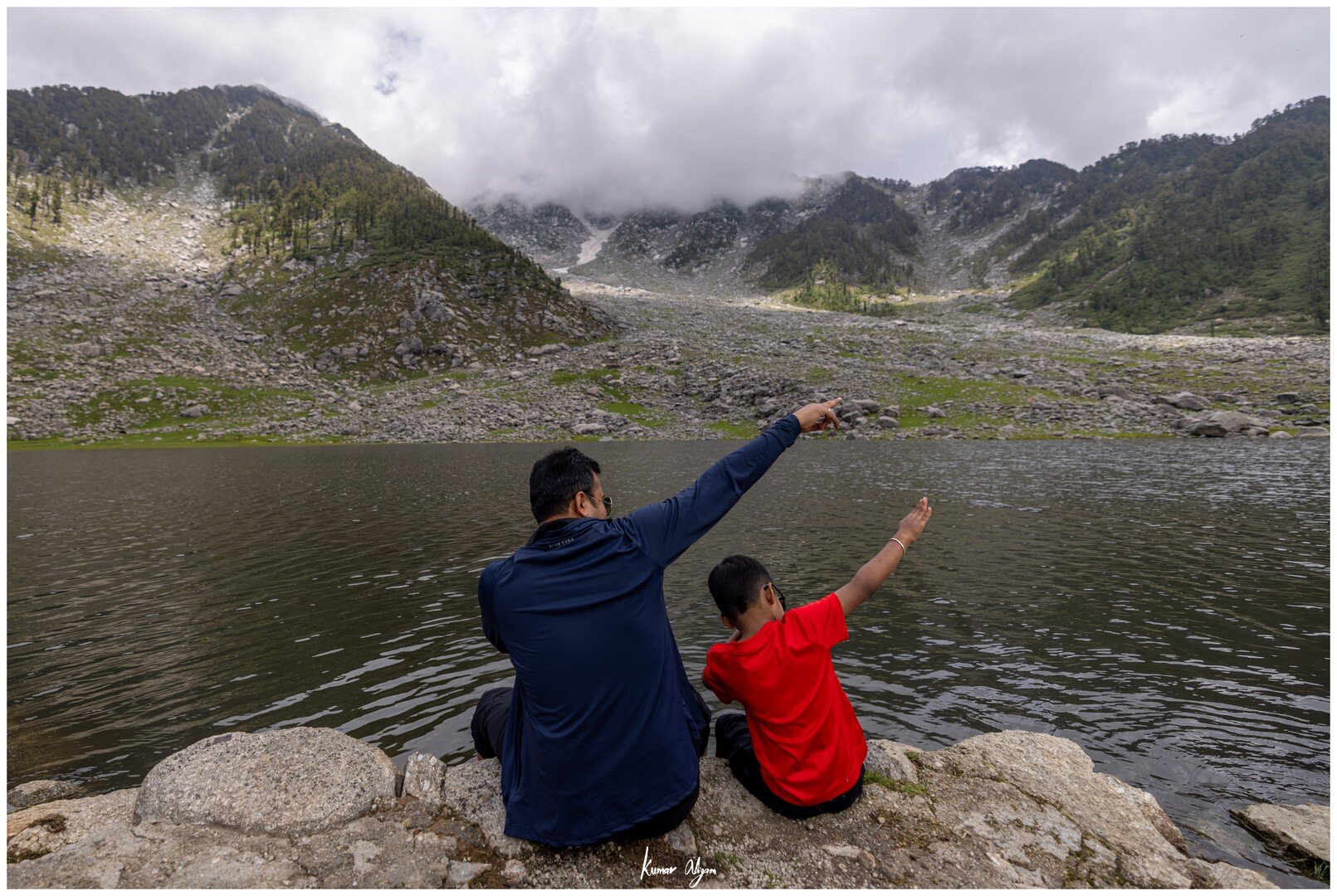 Yuvan and Papa sitting at the edge of the lake, pointing towards the mountains