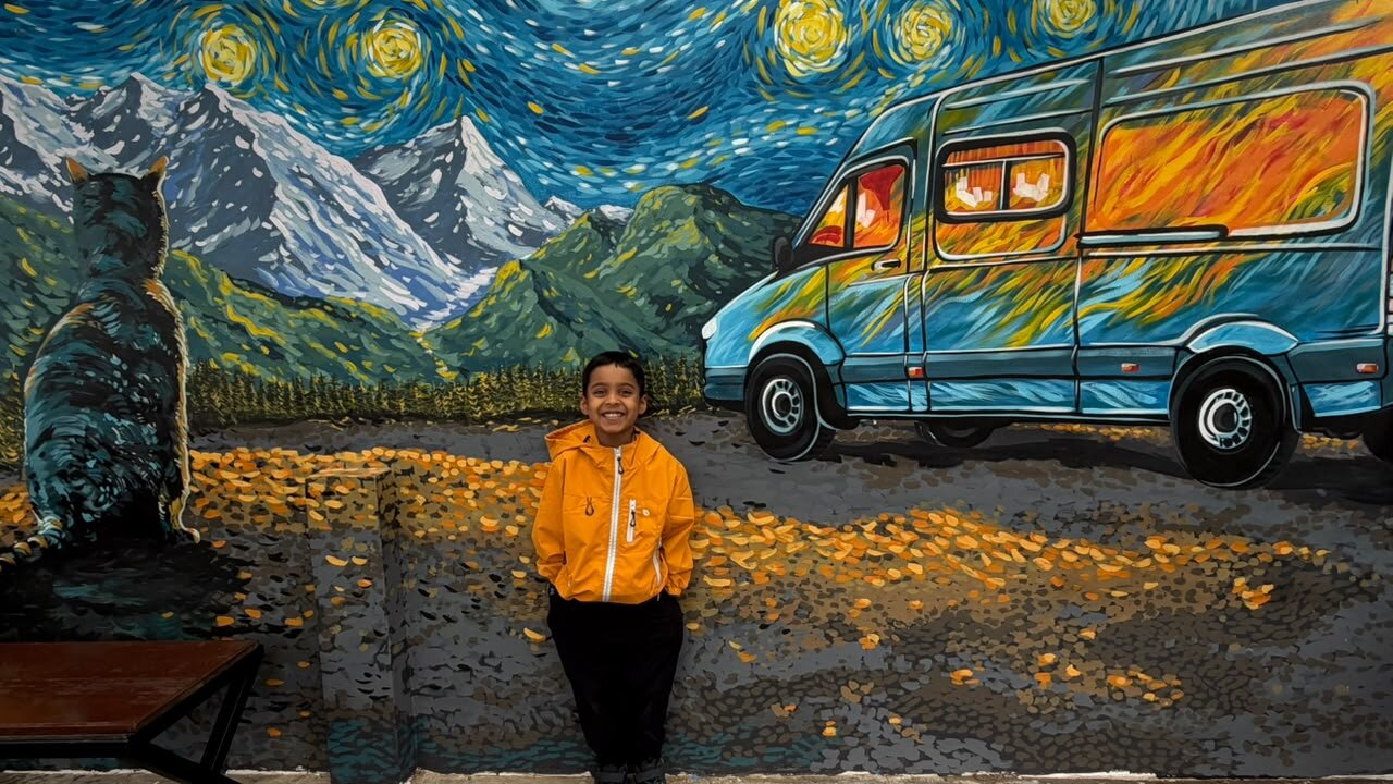 Yuvan smiling in front of a painted starry night mural of a mountain van